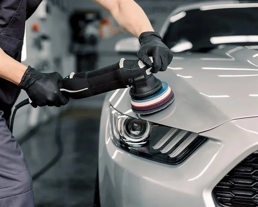 Technician machine-polishing a silver car at the studio
